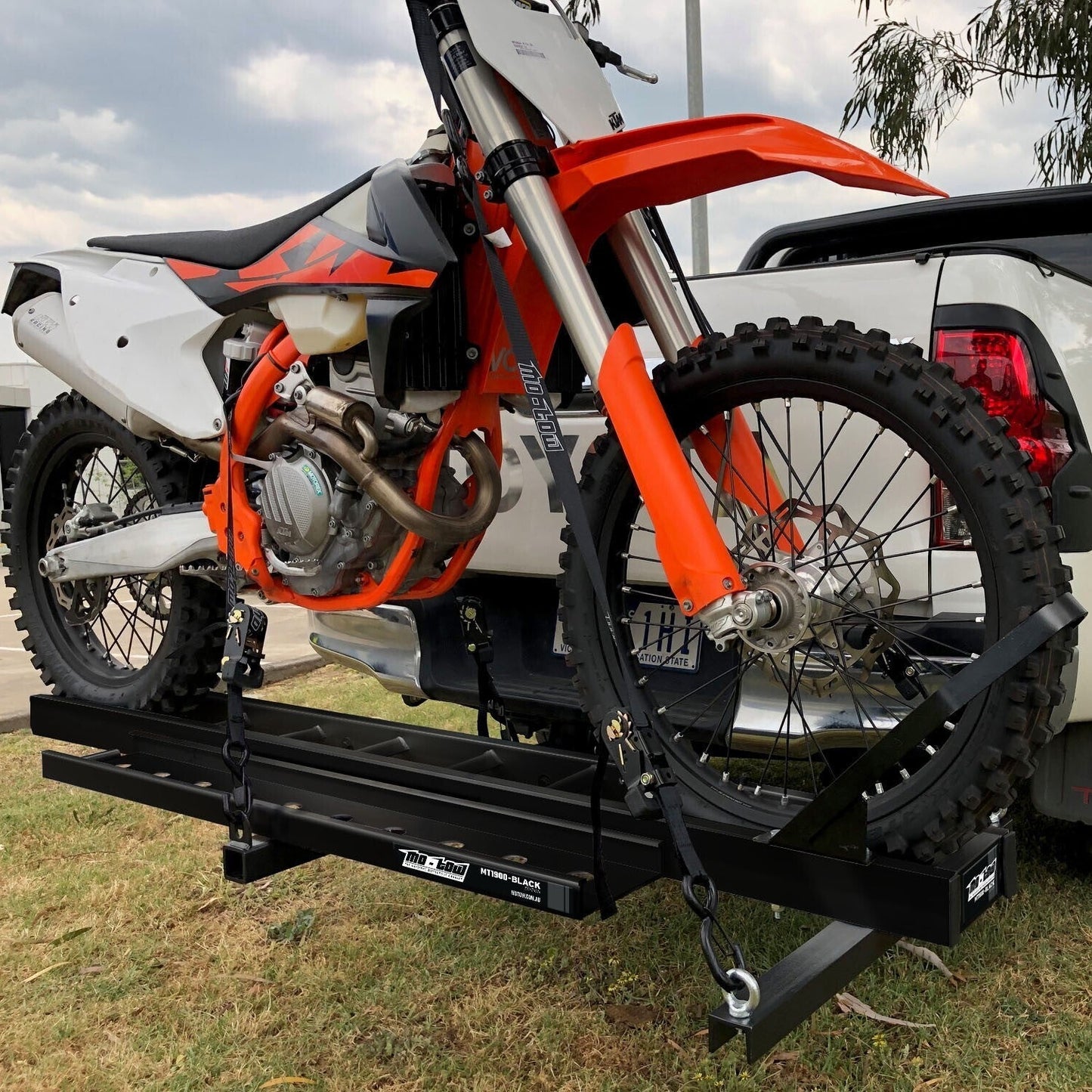 A black mo-tow 1.9M bike carrier attached to a vehicle, with a motocross bike secured on top of it.